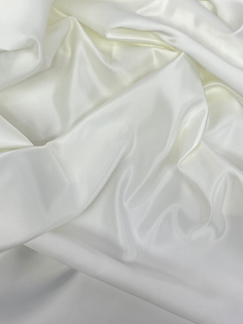 May include: White satin fabric with soft, flowing folds. The fabric is smooth and luxurious, with a subtle sheen.