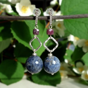 May include: A pair of silver dangle earrings with a blue gemstone bead, a square silver charm, and a small pink gemstone bead.