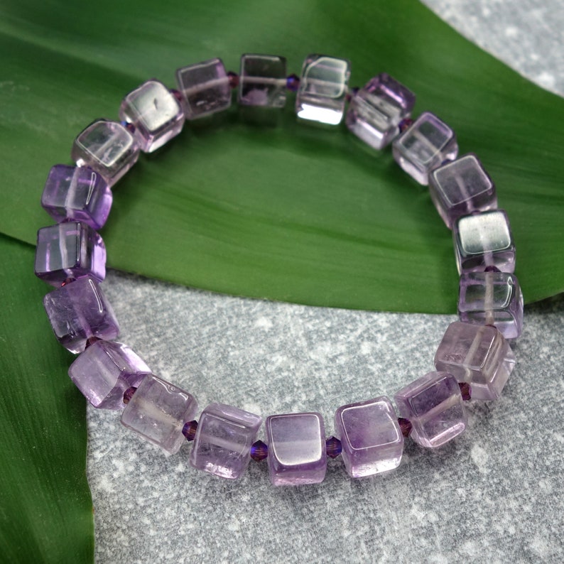 May include: A purple amethyst gemstone bracelet with square-shaped beads. The bracelet is made with faceted beads and is strung on elastic.