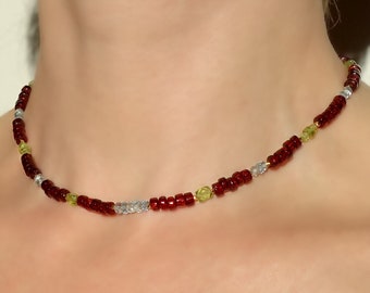 May include: A delicate choker necklace made with small red, green, and clear glass beads.