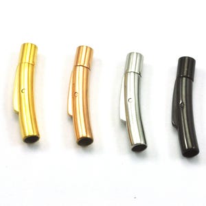 May include: Four curved magnetic clasps in gold, rose gold, silver, and black. Each clasp has a cylindrical barrel and a curved body with a small loop. The clasps are designed for jewellery making.