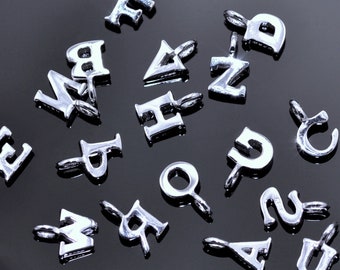 May include: A collection of silver letter charms, each with a different letter of the alphabet. The charms are arranged on a black background.