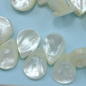 May include: A string of white pearlescent teardrop-shaped beads with a slightly iridescent sheen.