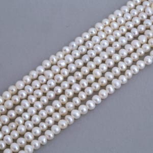 Può includere: Un filo di perle d'acqua dolce bianche, disposte in file, che mettono in mostra la loro forma rotonda e liscia e il loro delicato splendore.