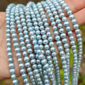 Può includere: Una collana di perle d'acqua dolce di colore azzurro chiaro. Le perle sono rotonde e lisce, e hanno un leggero bagliore iridescente.