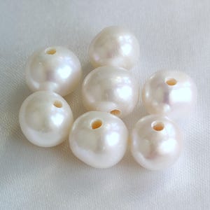 May include: Seven white round pearls with a hole drilled through the centre of each pearl.