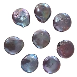 May include: Seven loose, flat, coin-shaped pearls with a dark, iridescent purple and grey lustre. Each pearl displays a unique, slightly irregular circular form with a smooth, reflective surface that catches light, showing subtle metallic undertones.