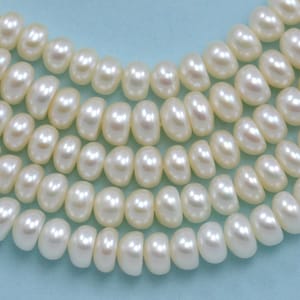 May include: A strand of white freshwater pearls, arranged in a circular pattern, showcasing their smooth, round shape and subtle lustre.