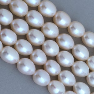 Peut inclure: Un brin de perles ovales blanches, disposées en rangées, mettant en valeur leur surface lisse et lustrée.