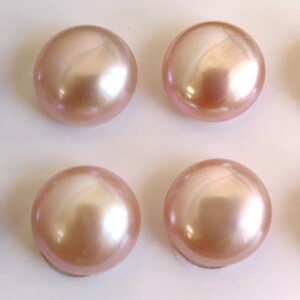 May include: Four round, smooth, pink pearls with a slight iridescent sheen. The pearls are arranged in a grid pattern on a white surface.
