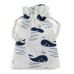 Può includere: Un piccolo sacchetto con coulisse bianco sporco con un motivo ripetuto di balene e onde blu navy. La borsa è realizzata in un tessuto strutturato e ha una chiusura con coulisse color naturale.