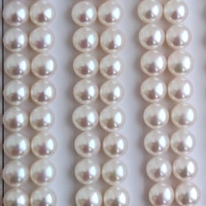 May include: A close-up of a row of white pearls, arranged in a grid pattern. The pearls are smooth and round, with a slight iridescent sheen.
