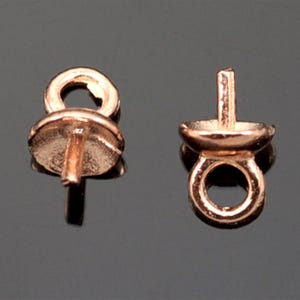 Könnte beinhalten: Zwei roségoldfarbene Metallperlenspitzen mit einer Öse an einem Ende und einem Stift am anderen Ende. Die Perlenspitzen sind für die Schmuckherstellung gedacht.
