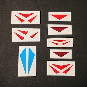 May include: Set of nine red and blue vinyl decals, featuring various geometric shapes, including triangles and diamonds. The decals are on white paper.
