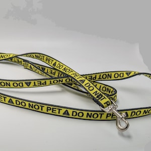 May include: A yellow and black leash with the text "DO NOT PET" repeated along the length. The leash has a silver clip.