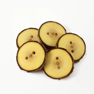 May include: A group of six wooden buttons with a natural wood finish. The buttons are round and have a hole in the center. The buttons are arranged in a pile.