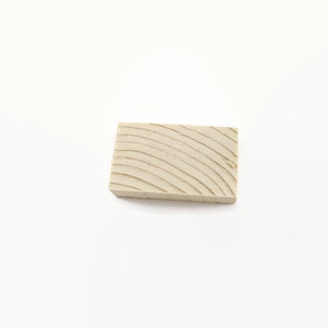 May include: A small, rectangular block of wood with a light brown color and a grain pattern.