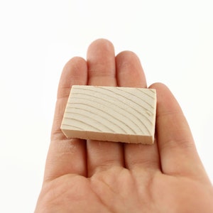 May include: A small, rectangular block of wood with a light brown color and a grain pattern. The block is smooth and has a slightly rounded edge.