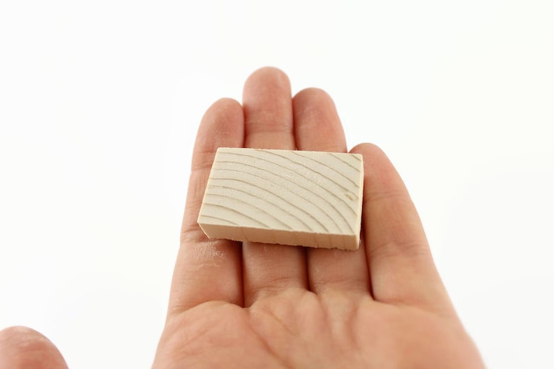 May include: A small, rectangular block of wood with a light brown color and a grain pattern. The block is smooth and has a slightly rounded edge.