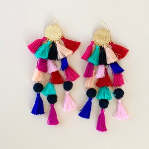 Puede incluir: Un par de pendientes de borla coloridos con tapas circulares doradas. Las borlas est&aacute;n hechas de varios colores, incluyendo rosa, rojo, azul, verde y negro.