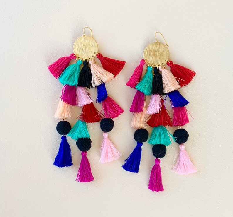 Puede incluir: Un par de pendientes de borla coloridos con tapas circulares doradas. Las borlas est&aacute;n hechas de varios colores, incluyendo rosa, rojo, azul, verde y negro.