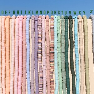 May include: A collection of 26 strands of colourful polymer clay beads, labelled with letters A through Z, and two additional strands labelled 2 and 3. The beads are all round and flat, and they are arranged in a row against a white background.
