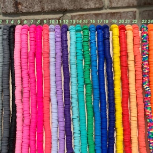 May include: A set of 25 colourful round polymer clay beads, each strung on a separate thread. The beads are arranged in a row, numbered 1 through 25. The beads are various colours, including black, grey, pink, red, orange, yellow, green, blue, and purple.