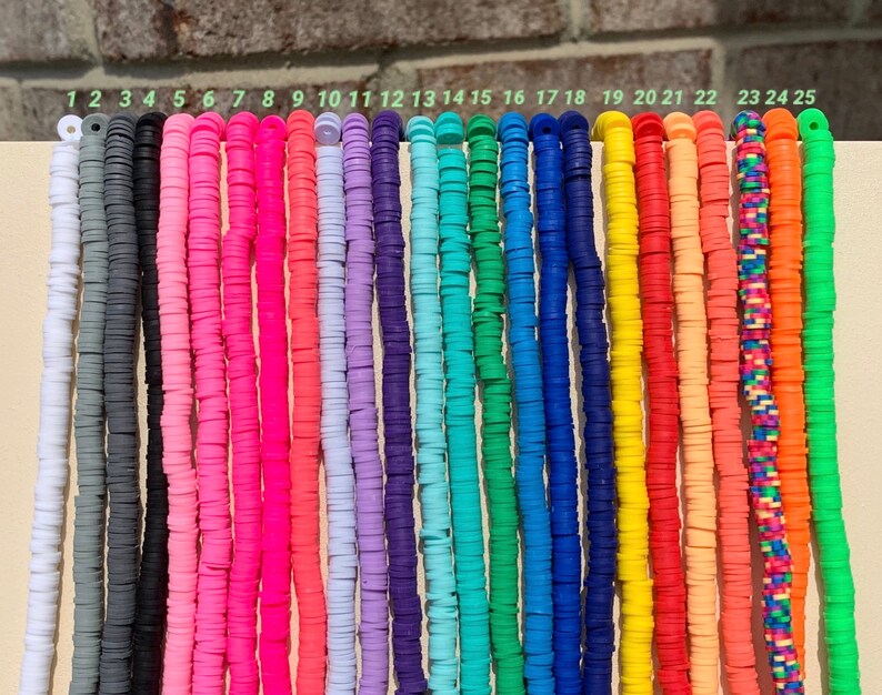 May include: A set of 25 colourful round polymer clay beads, each strung on a separate thread. The beads are arranged in a row, numbered 1 through 25. The beads are various colours, including black, grey, pink, red, orange, yellow, green, blue, and purple.
