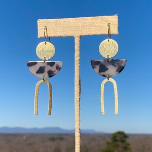 May include: Gold and white geometric earrings with a half-circle, circle, and arch design.