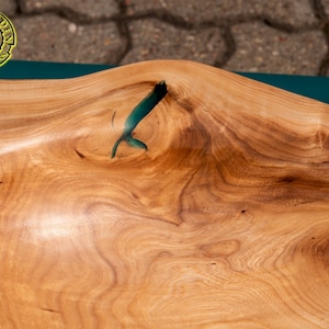 K&ouml;nnte beinhalten: Nahaufnahme einer Tischplatte aus Holz mit nat&uuml;rlicher Holzmaserung. Die Tischplatte hat eine F&uuml;llung aus tealblauem Epoxidharz in einem Riss im Holz.