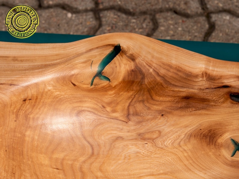 K&ouml;nnte beinhalten: Nahaufnahme einer Tischplatte aus Holz mit nat&uuml;rlicher Holzmaserung. Die Tischplatte hat eine F&uuml;llung aus tealblauem Epoxidharz in einem Riss im Holz.