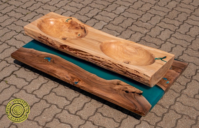 K&ouml;nnte beinhalten: Ein Doppelwaschtisch aus einer gro&szlig;en, nat&uuml;rlichen Holzplatte mit zwei ausgeh&ouml;hlten Becken. Das Holz hat eine nat&uuml;rliche, rustikale Oberfl&auml;che und steht auf einem Sockel aus dem gleichen Holz mit einer Einlage aus tealblauem Epoxidharz.