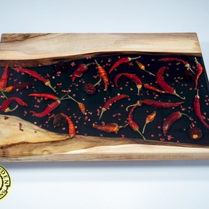 May include: A wooden serving board with a black epoxy resin inlay featuring red chili peppers and pink peppercorns.