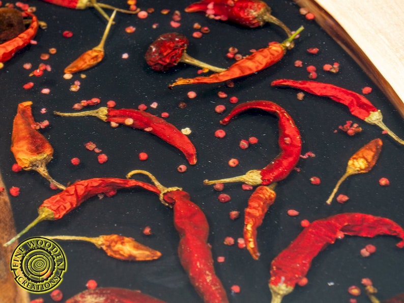 May include: A close-up of a black resin tray with red chili peppers and pink peppercorns. The tray is round and has a wooden edge.