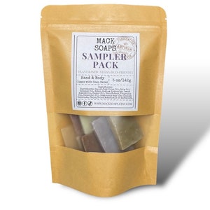 May include: A brown paper bag with a clear window displaying a sampler pack of soaps. The label reads "MACK SOAPS SAMPLER PACK" and lists ingredients. The pack contains 5 oz / 142g of soap. The soaps are various colors and shapes.