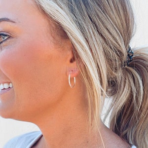 May include: A close-up of a person's ear wearing a pair of silver hoop earrings.