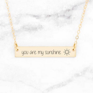 以下が含まれることがあります： 「you are my sunshine」という刻印と小さな太陽のアイコンが付いたゴールドバーネックレス