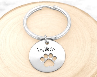 May include: Silver key chain with a round tag that says "Willow" and has a paw print cut out. The key chain is on a wooden surface.