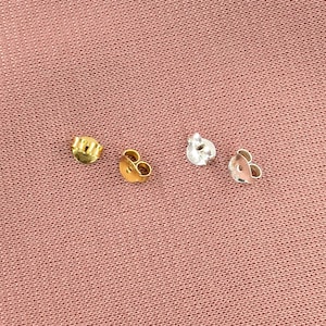 May include: Four earring backs, two gold and two silver, on a pink fabric background.