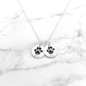 May include: Silver necklace with two round pendants featuring paw prints and the names "Sammy" and "Buster".