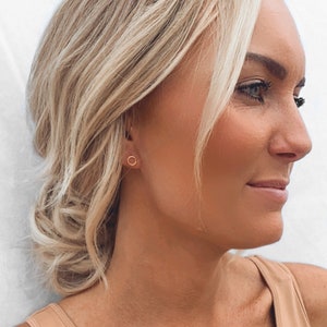 May include: A close-up of a woman's ear with a small gold hoop earring. The earring is simple and delicate, and it is a popular choice for everyday wear.