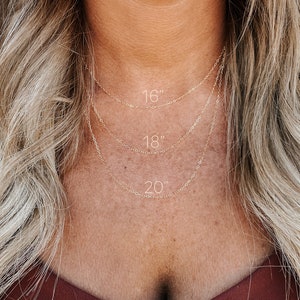 May include: Three gold chain necklaces layered on a person's neck. The chains are labeled with their lengths: 16 inches, 18 inches, and 20 inches.