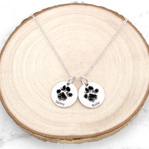 May include: Silver necklace with two round pendants featuring paw prints and the names "Sammy" and "Buster" engraved on them.
