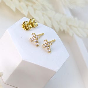 May include: A pair of gold cross stud earrings with small clear cubic zirconia stones.