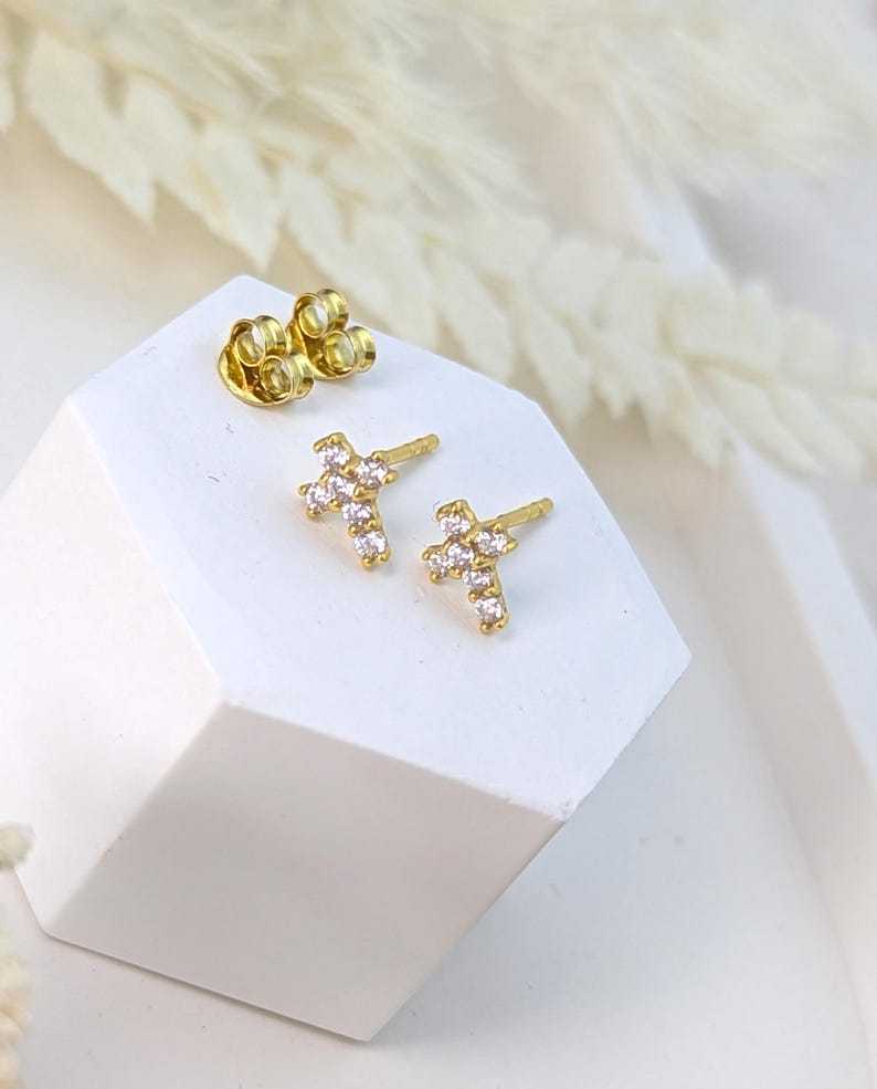 May include: A pair of gold cross stud earrings with small clear cubic zirconia stones.