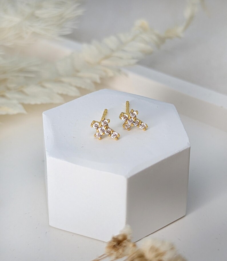 May include: A pair of gold cross earrings with clear cubic zirconia stones.