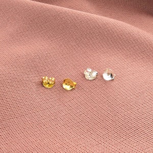 May include: Four earring backs, two gold and two silver, on a pink fabric background.