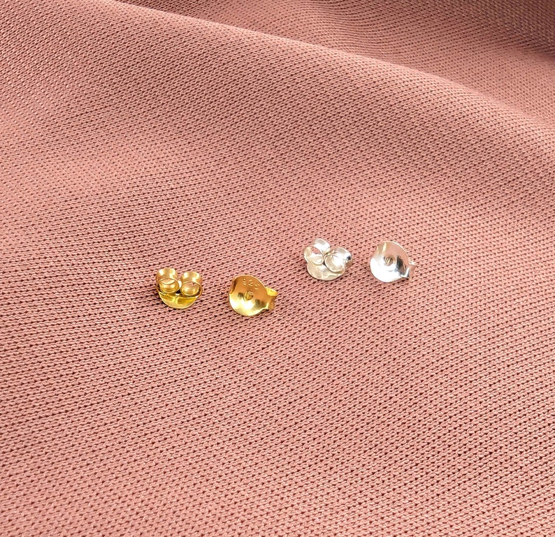 May include: Four earring backs, two gold and two silver, on a pink fabric background.