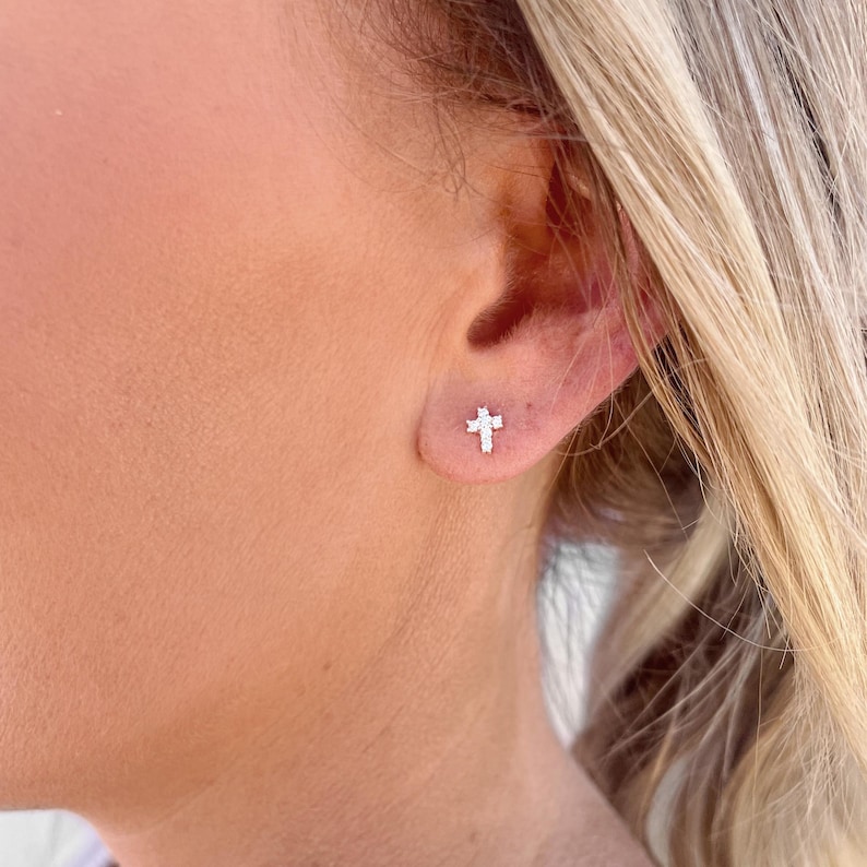 May include: A pair of small, silver cross stud earrings with clear cubic zirconia stones.