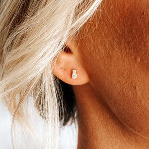 May include: A close-up of a person's ear with a small, silver stud earring featuring a single, clear gemstone.